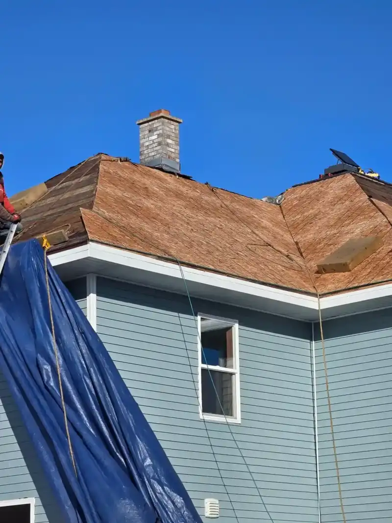 Roof deck exposed during tear-off on a blue Wisconsin home with chimney detail