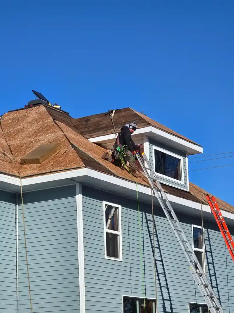 AM Exteriors crew member working on a steep roof tear-off on a blue Wisconsin home