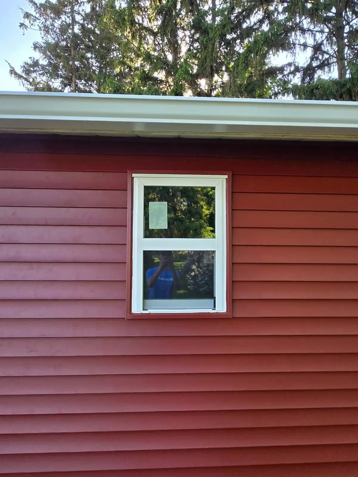Close up of a new white double-hung window installed in red lap siding with clean white trim and gutter above