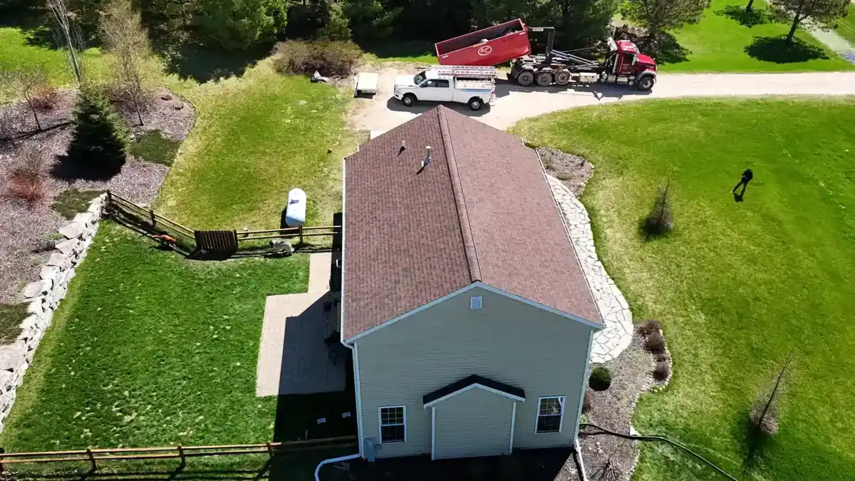 Aerial view of a finished shingle roof with AM Exteriors truck and dump trailer on the jobsite