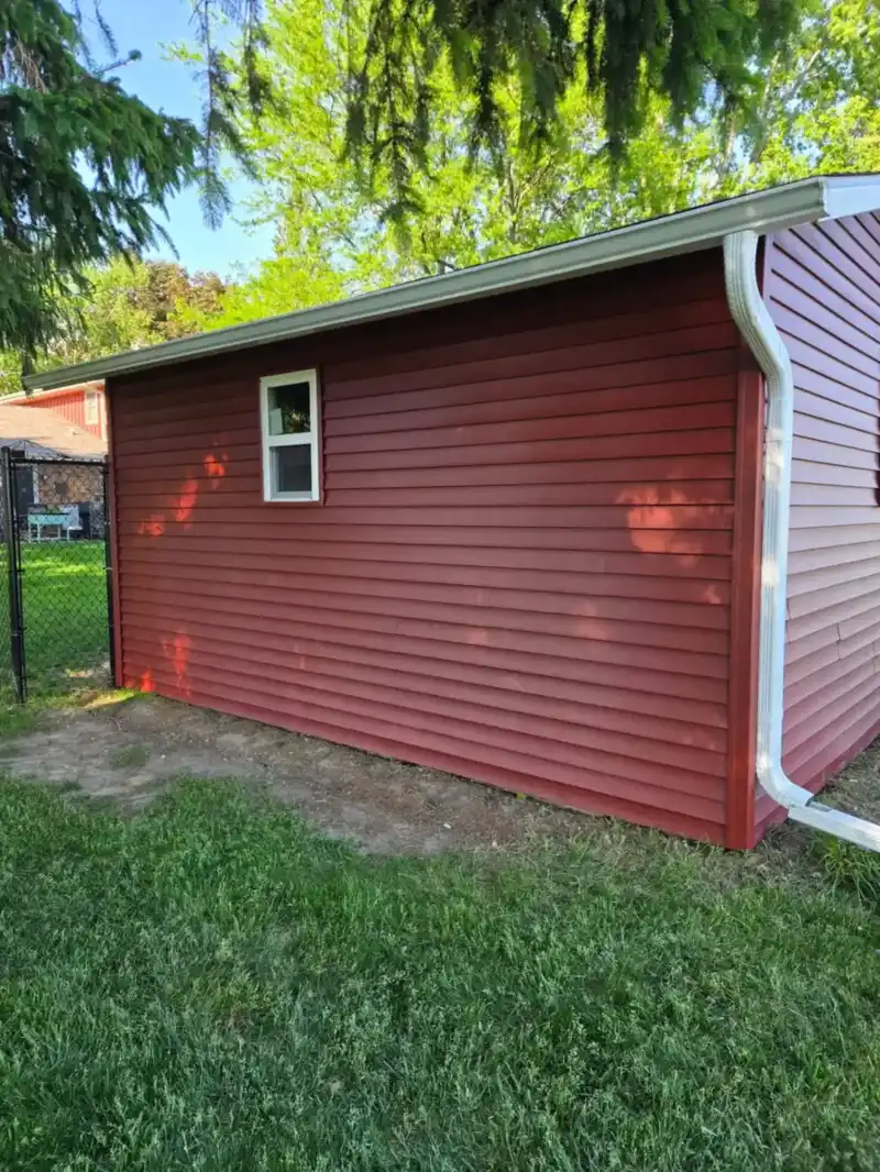 Red lap siding on a detached garage side wall with new white seamless gutter and downspout in Wisconsin
