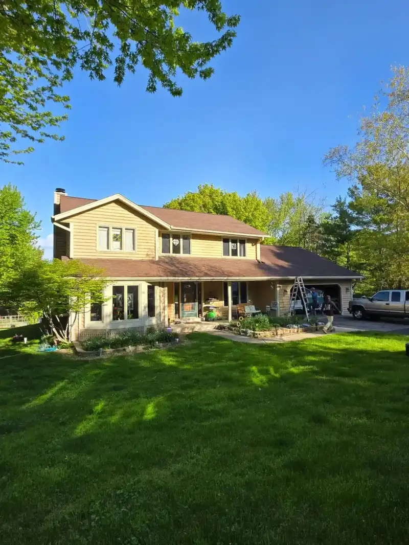 Wide front view of a tan Wisconsin two-story home with AM Exteriors team on site during an exterior remodel