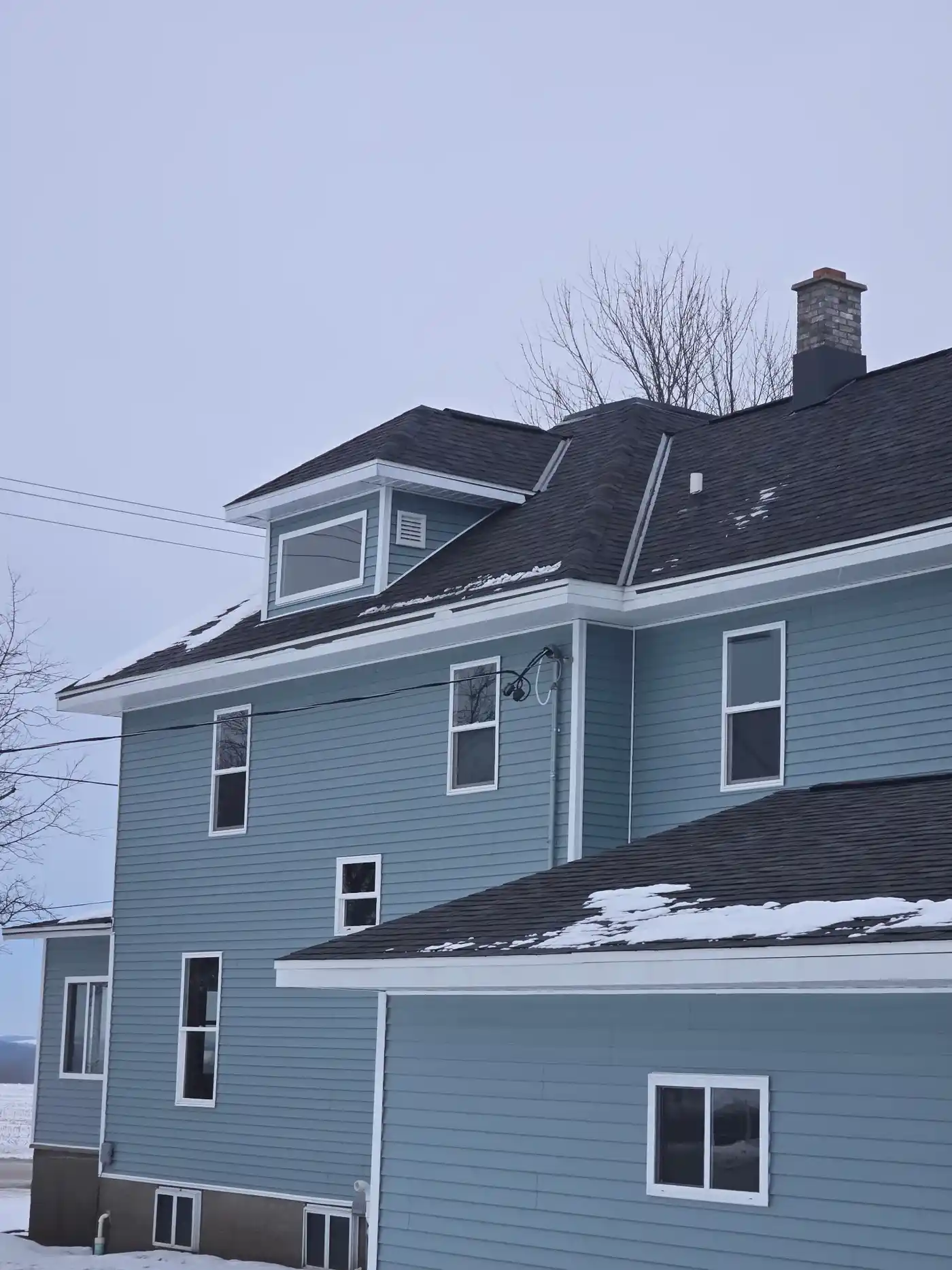 Side view of a completed dark shingle roof on a blue Wisconsin home with dormer and chimney