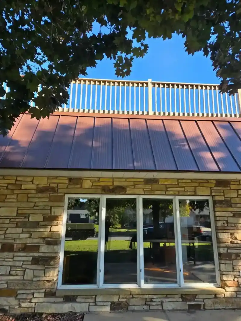 Copper standing-seam metal roof on a stone home with rooftop deck railing