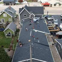 Wide aerial view of a large reroof project with multiple crew members working on a dark shingle roof