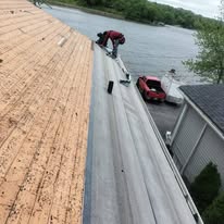 Crew member installing membrane on a low-slope roof beside a lakefront home