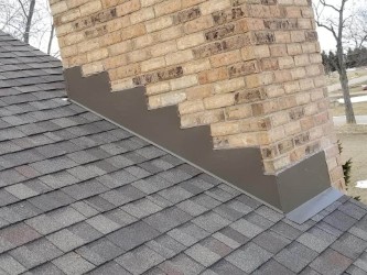 Close-up of new chimney step flashing and counter flashing integrated into an asphalt shingle roof